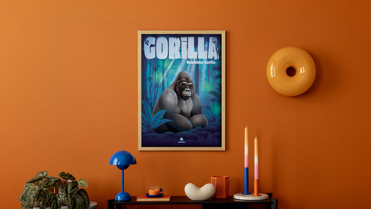Ein illustriertes Tier-Plakat mit einem sitzenden Gorilla in einer bläulichen Wald-Szenerie, hängt an einer Wand in einem orangenen Wohnzimmer mit moderner Einrichtung.