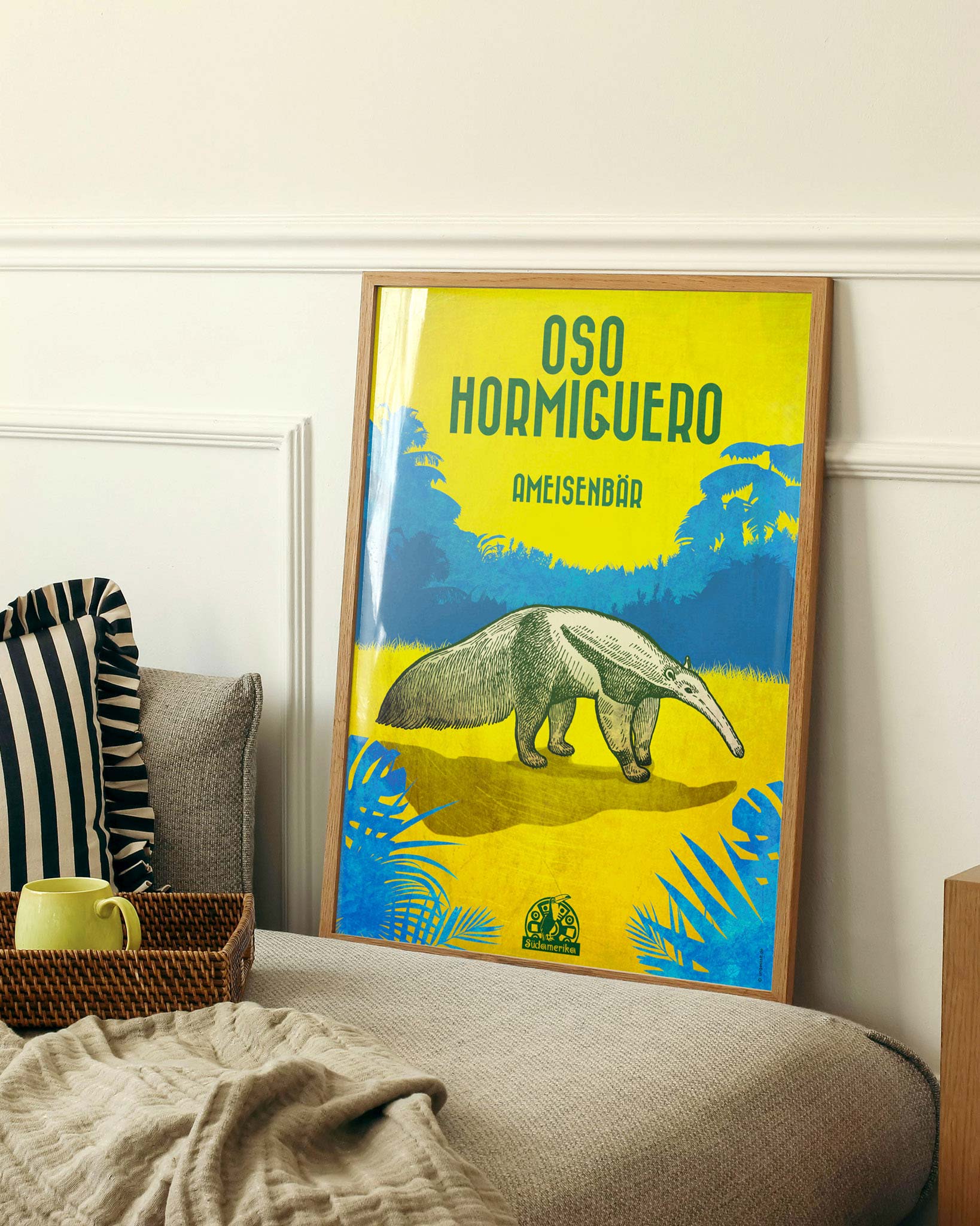 Gerahmtes Poster neben einem Bett mit einem Ameisenbär in blauen und gelben Farben