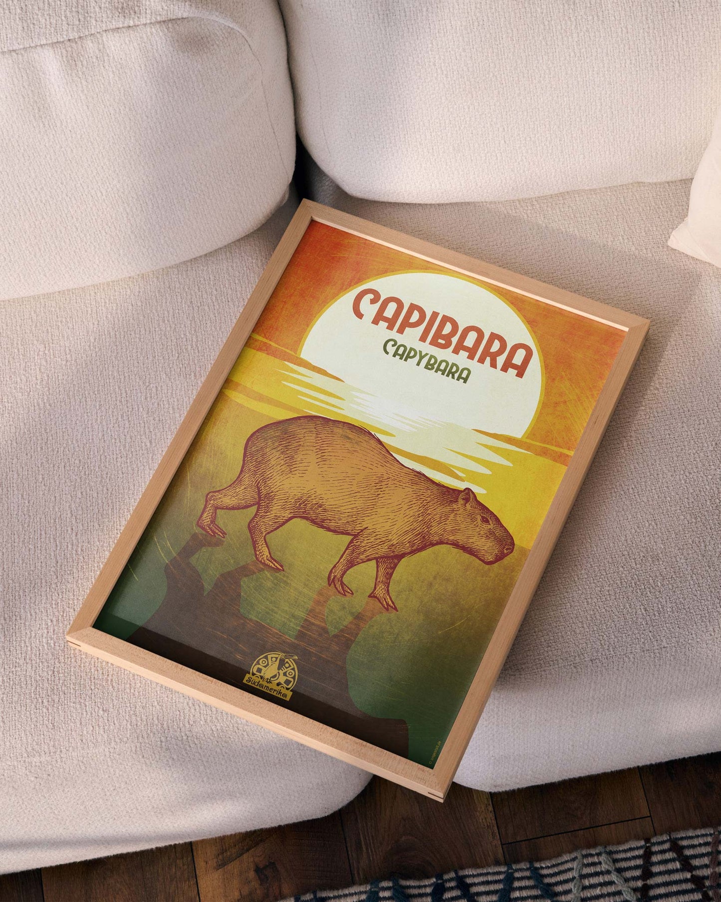 Gerahmtes Poster auf einem Sofa liegend mit einem Capybara vor Sonnenuntergang